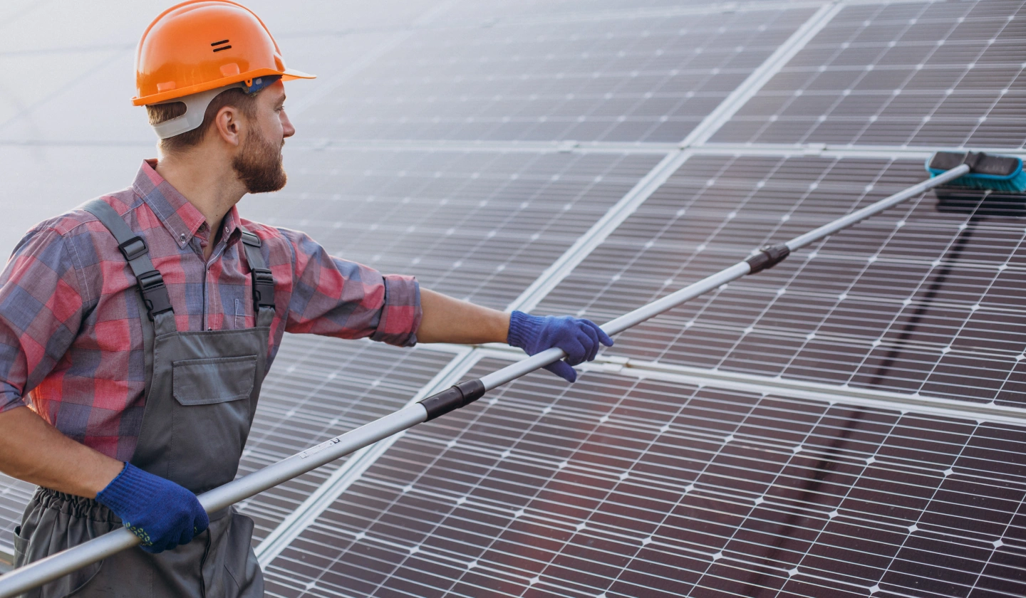 Operario limpiando módulos fotovoltaicos con una pértiga y un cepillo