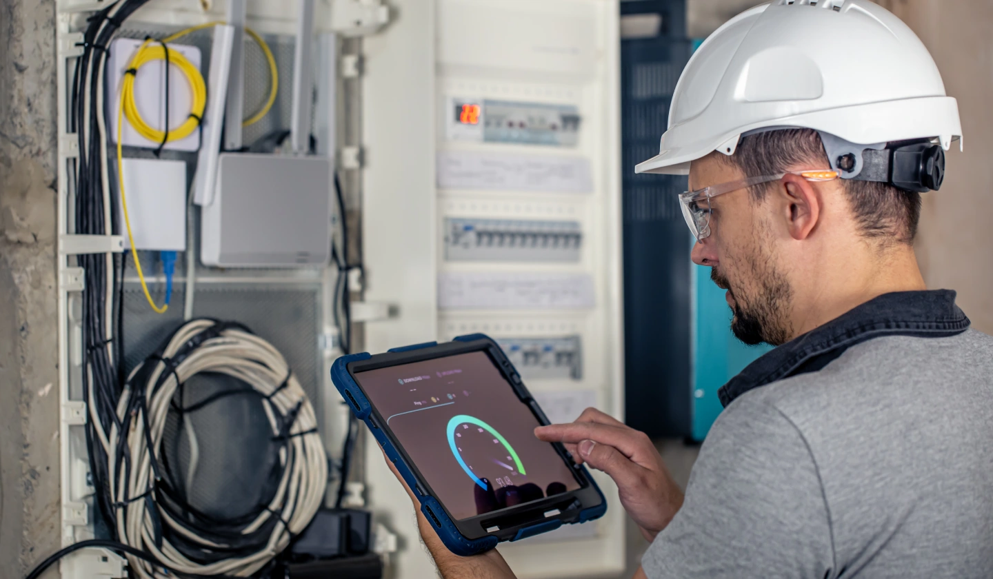 Técnico con casco ante un cuadro eléctrico abierto consultando la monitorización en una tablet