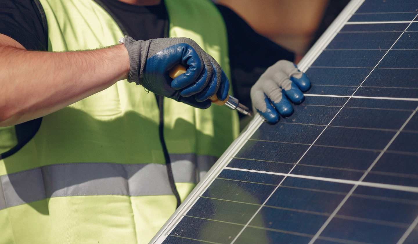 Instalador con guantes trabajando con un destornillador sobre el marco de un panel solar